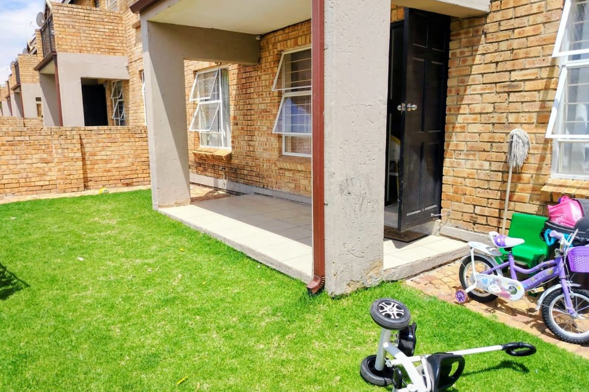 A rear view of the townhouse featuring a covered tiled patio, face-brick exterior walls, and access to a private garden area.