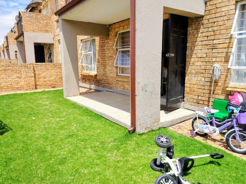 A rear view of the townhouse featuring a covered tiled patio, face-brick exterior walls, and access to a private garden area.