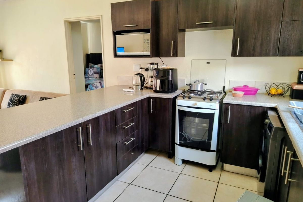 A functional kitchen featuring dark wood-look cabinetry, light countertops, and a gas stove, with an open-plan layout connecting to the adjacent living area.