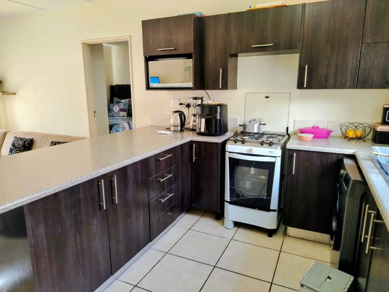 A functional kitchen featuring dark wood-look cabinetry, light countertops, and a gas stove, with an open-plan layout connecting to the adjacent living area.