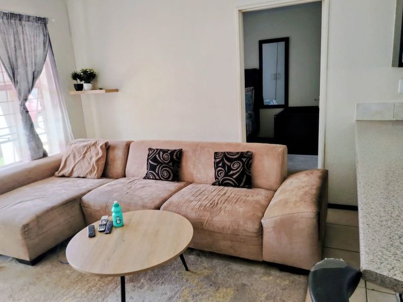 A living room area featuring tiled flooring and a window with a curtain rail, providing access to an adjacent room.
