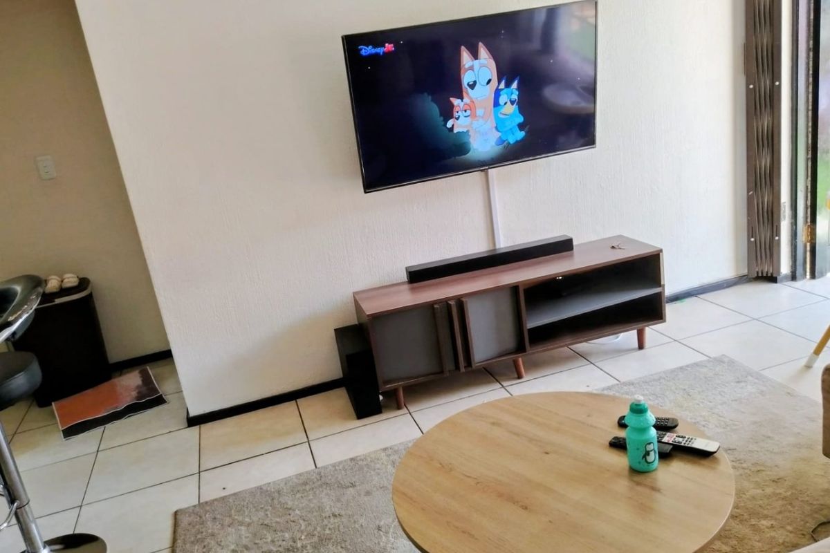 A living room area featuring tiled flooring and a wall-mounted television setup, providing a functional space for relaxation.