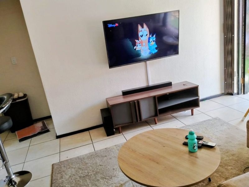 A living room area featuring tiled flooring and a wall-mounted television setup, providing a functional space for relaxation.