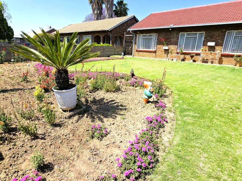 A well-maintained rear garden featuring a manicured lawn, established flower beds, and a classic brick house exterior with a tiled roof.
