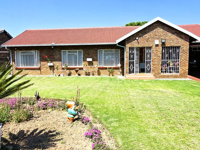 A well-maintained single-story face brick home featuring a tiled roof, secure window bars, and an attached carport set within a neat garden.