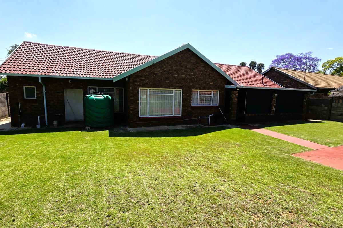 Rear view of a brick house featuring a tiled roof, a green water storage tank, and a well-maintained lawn area.
