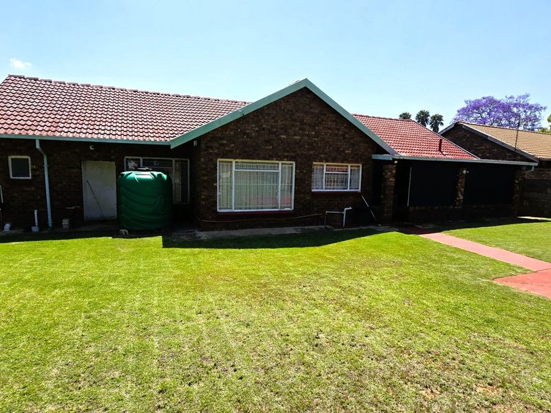 Rear view of a brick house featuring a tiled roof, a green water storage tank, and a well-maintained lawn area.