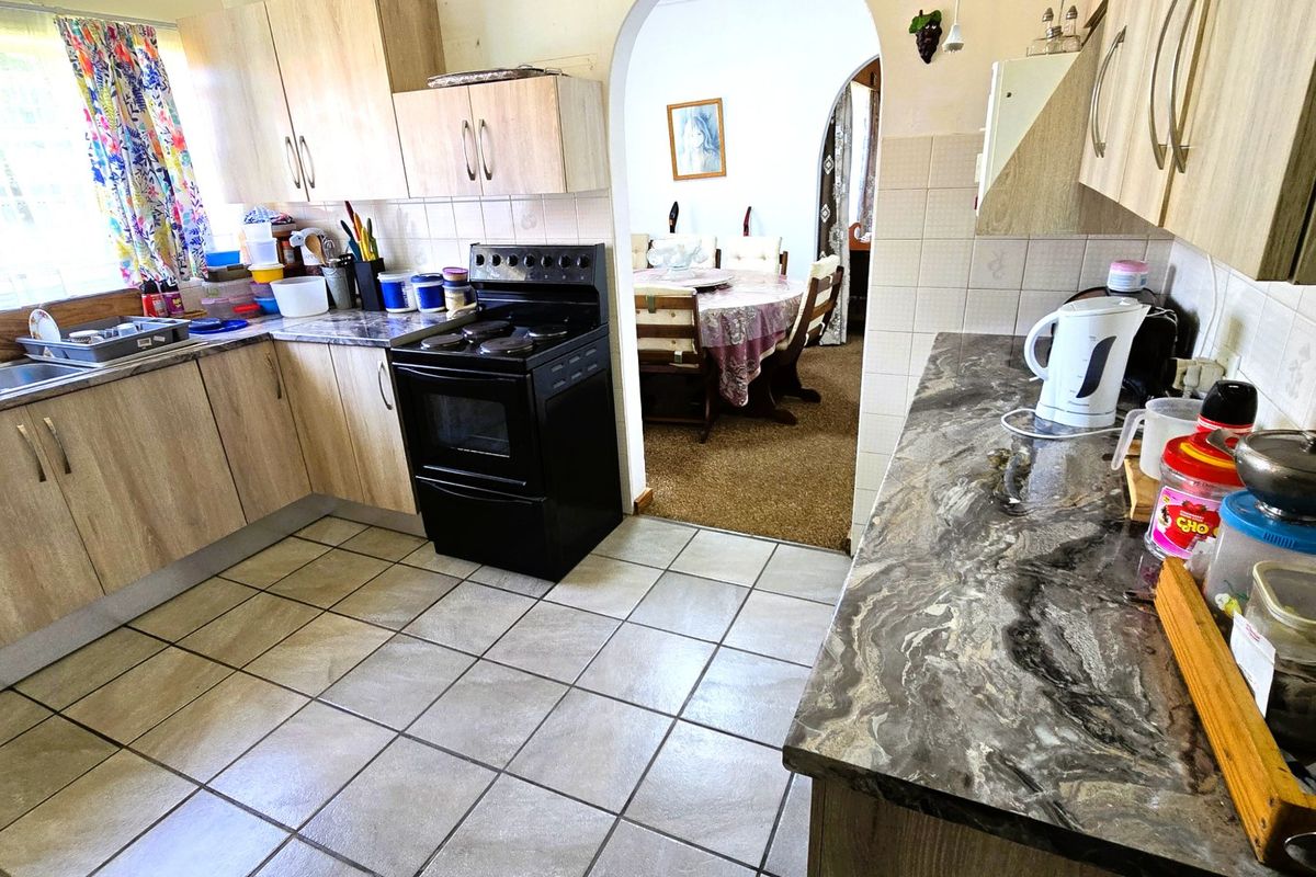 Functional kitchen featuring laminate cabinetry, stone-look countertops, and tiled flooring, with an open archway leading to the adjacent dining area.