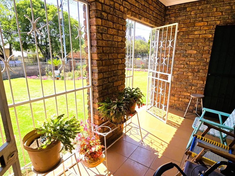 A covered patio area featuring exposed brick walls, tiled flooring, and security gates, offering a view of the garden.