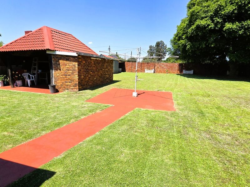 Spacious backyard featuring a large lawn, a covered brick patio area, and a concrete pathway leading to a rotary clothesline.