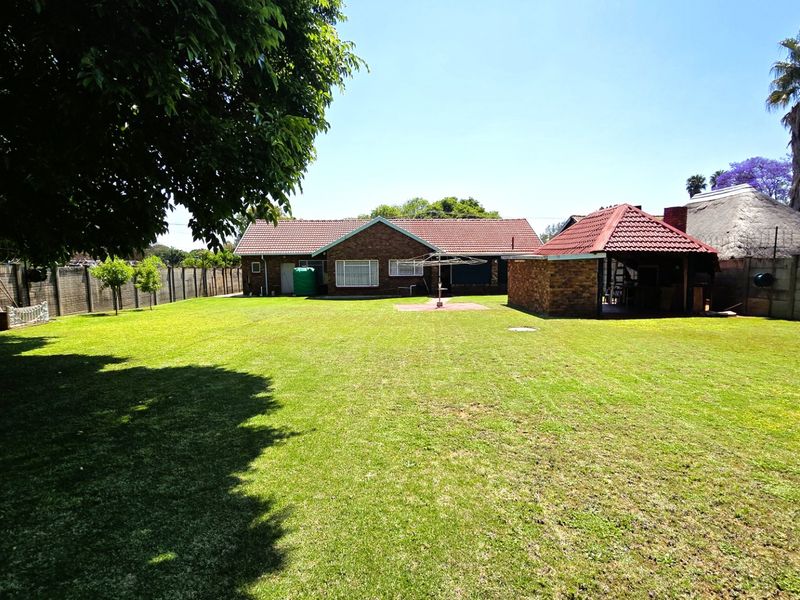 Spacious rear garden featuring a large lawn, brick-built house with a tiled roof, and a separate thatched outdoor entertainment structure.