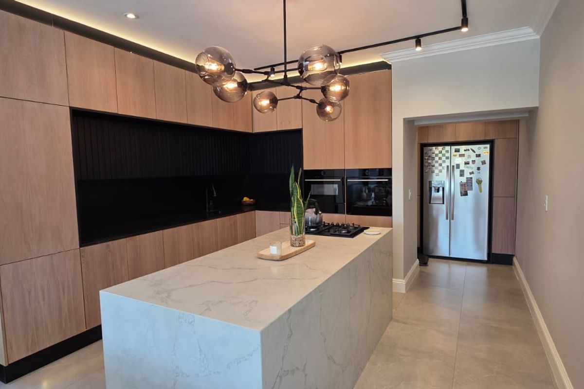 Modern kitchen featuring a large stone-topped island, sleek wood-finish cabinetry, integrated appliances, and contemporary lighting, offering a clean and functional culinary space.