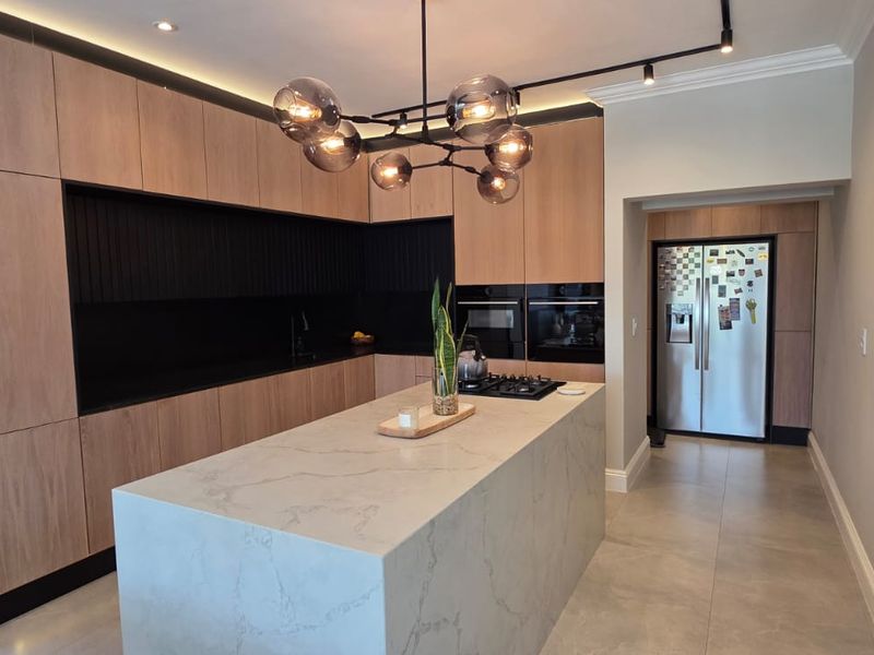Modern kitchen featuring a large stone-topped island, sleek wood-finish cabinetry, integrated appliances, and contemporary lighting, offering a clean and functional culinary space.