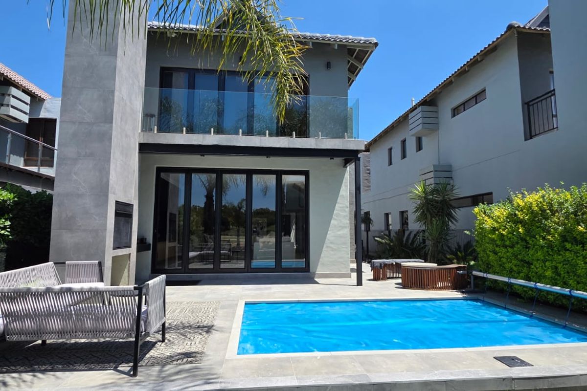 Rear view of a modern two-story home featuring a swimming pool, tiled patio, outdoor fireplace, and large bi-fold doors leading to the interior.