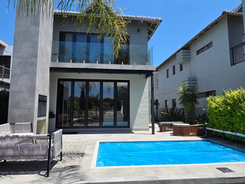 Rear view of a modern two-story home featuring a swimming pool, tiled patio, outdoor fireplace, and large bi-fold doors leading to the interior.