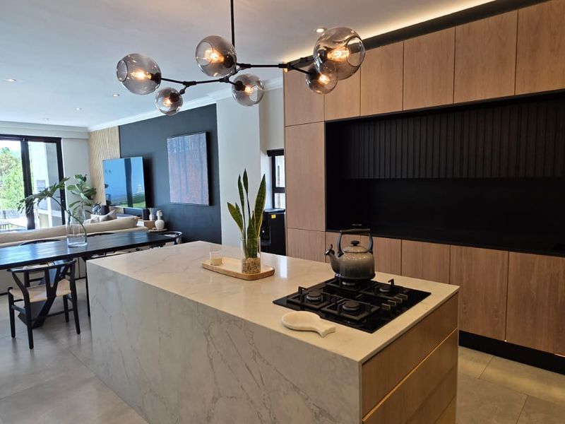 Modern open-plan living area featuring a sleek kitchen with a stone island, gas cooktop, and seamless flow to the outdoor patio through sliding doors.