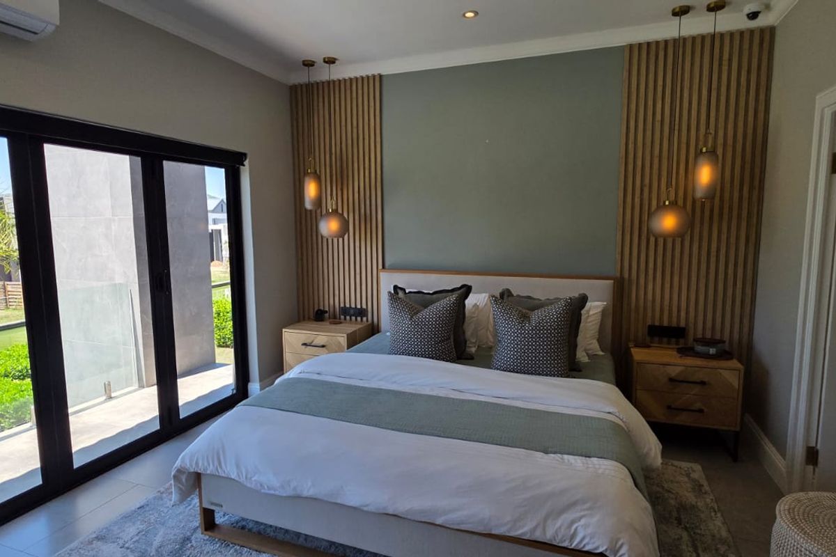 Modern bedroom featuring stylish timber slat wall paneling, pendant lighting, and large sliding glass doors providing access to an outdoor area.