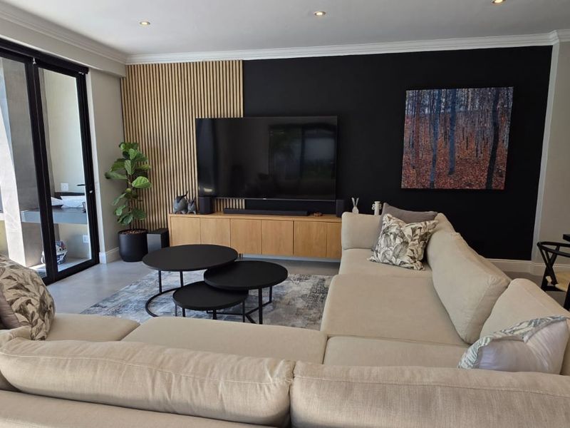 Modern open-plan living area featuring a stylish timber slat feature wall, recessed lighting, and large sliding doors providing seamless access to the outdoor patio.