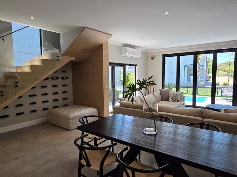 Modern open-plan living and dining area featuring a striking floating staircase with glass balustrade, built-in wine storage, and seamless access to the outdoor pool area.