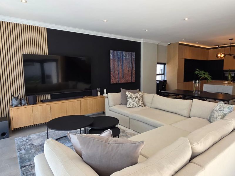 Modern open-plan living area featuring a stylish slatted timber feature wall, recessed lighting, and a contemporary kitchen with integrated appliances and a central island.
