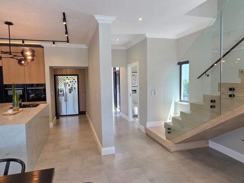 Modern open-plan kitchen featuring a stone island, timber cabinetry, and a striking glass-railed staircase, creating a seamless and contemporary living space.