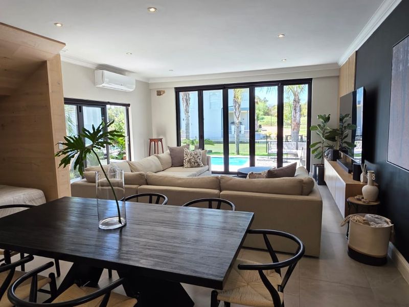 Spacious open-plan living and dining area featuring modern tiled floors, recessed lighting, a built-in wine rack, and bi-fold doors opening to the pool area.