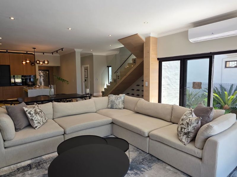 Spacious open-plan living area featuring a modern kitchen, timber staircase with glass balustrade, and bi-fold doors leading to the exterior.