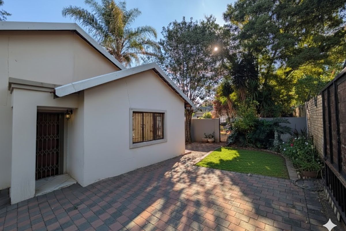 Rear exterior view of the property featuring a paved patio area, small lawn, and secure access points with security gates and window bars.