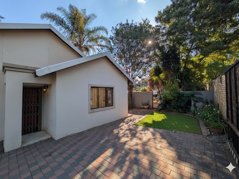 Rear exterior view of the property featuring a paved patio area, small lawn, and secure access points with security gates and window bars.