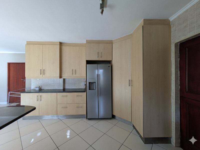 A functional kitchen featuring light wood-finish cabinetry, stone countertops, tiled backsplash, and neutral floor tiles, offering a clean and practical workspace.