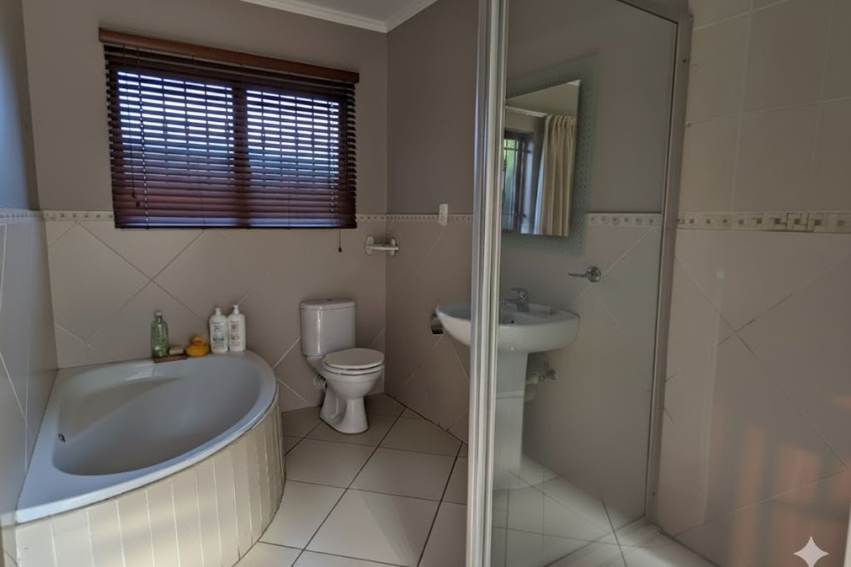 A functional bathroom featuring a corner bathtub, pedestal basin, toilet, and a separate shower enclosure with neutral wall and floor tiling.