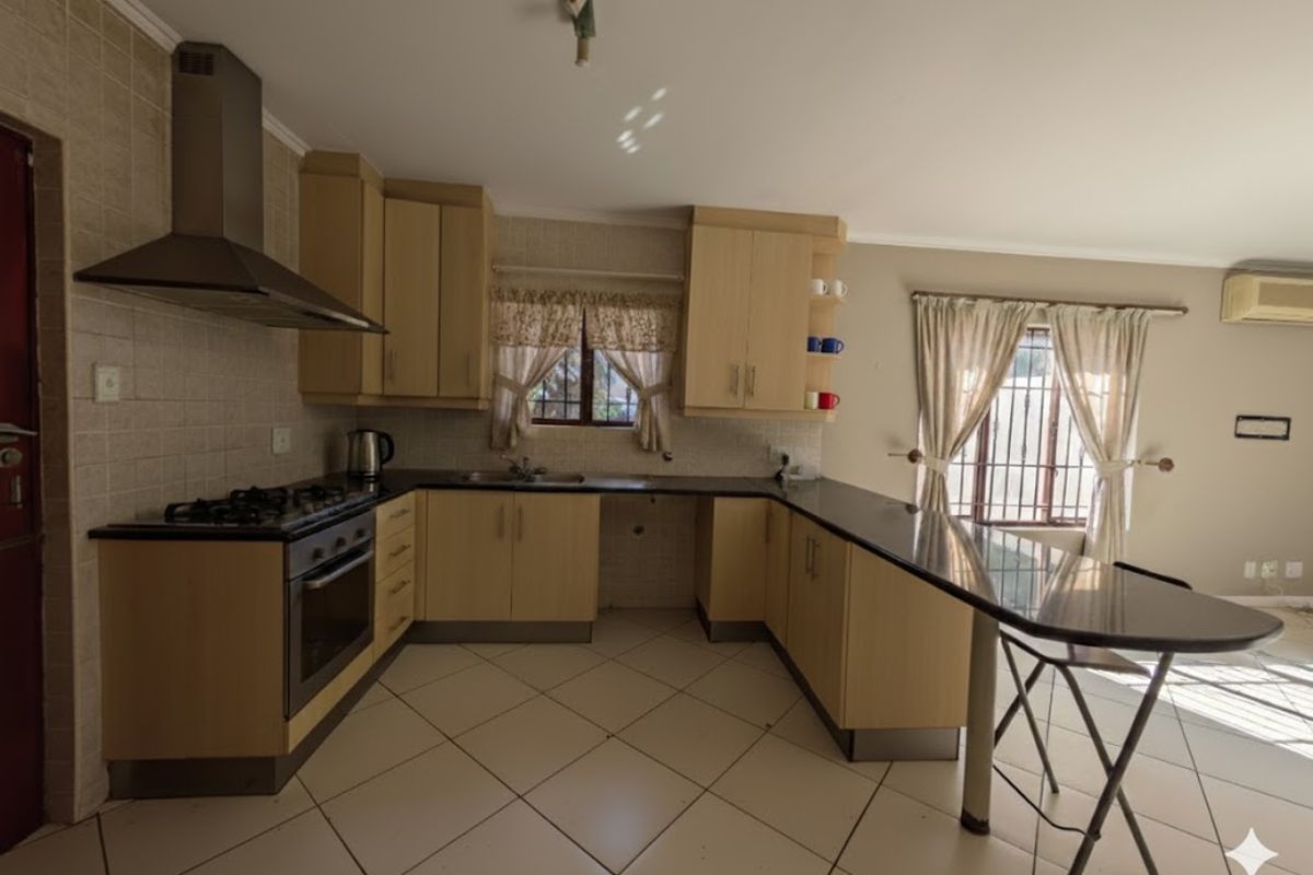Functional kitchen featuring light wood cabinetry, dark countertops, a gas hob with extractor, and a breakfast bar, with tiled flooring throughout.