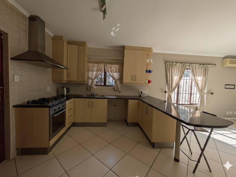 Functional kitchen featuring light wood cabinetry, dark countertops, a gas hob with extractor, and a breakfast bar, with tiled flooring throughout.