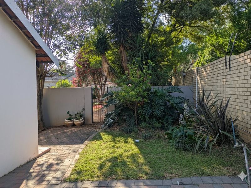 A private rear garden area featuring a paved walkway, established landscaping, and secure brick boundary walls with electric fencing.
