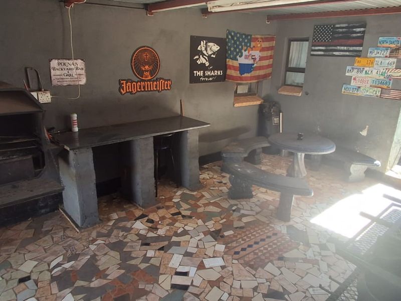 Covered outdoor patio area featuring a built-in braai, stone tile flooring, and a concrete prep counter, ideal for outdoor entertaining.