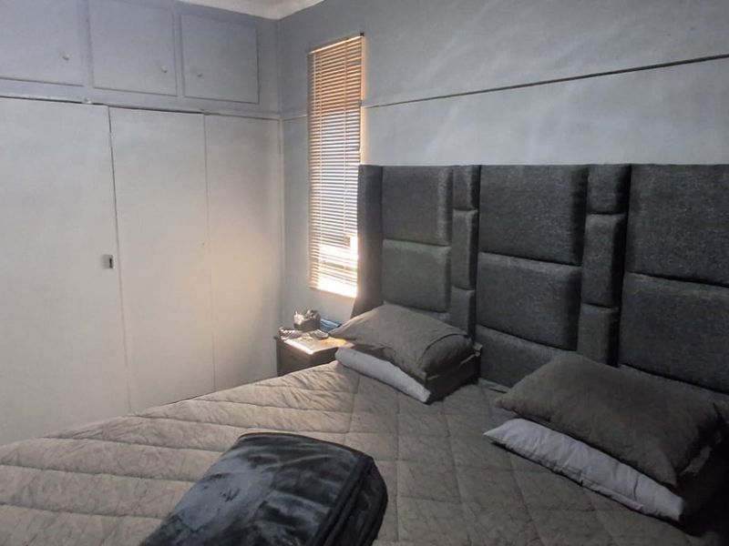 A bedroom featuring built-in cupboards with overhead storage, a picture rail, and a window fitted with a venetian blind.