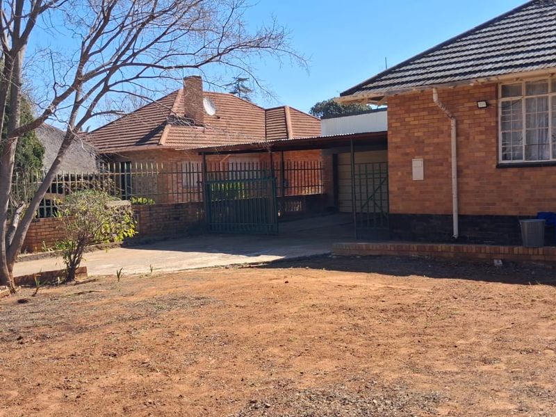 Front view of a brick house featuring a carport, metal security gate, and a large open yard area.