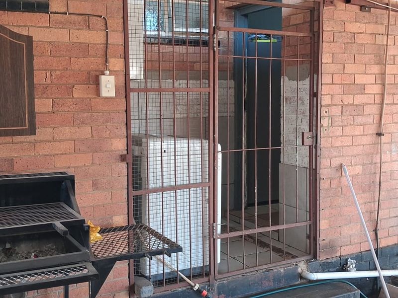 Covered patio area featuring a built-in braai, security gate access, and exposed brick walls, offering potential for an outdoor entertainment space.