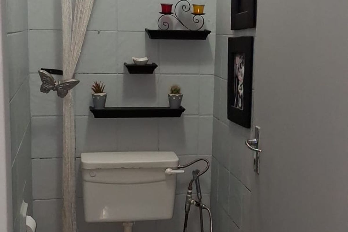 A compact guest bathroom featuring dated ceramic wall and floor tiles, a standard toilet, and a small window with security bars.