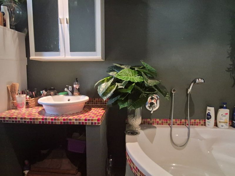 Bathroom featuring a corner bathtub with handheld shower, a vessel sink set on a mosaic-tiled vanity, and wall-mounted storage cabinetry.