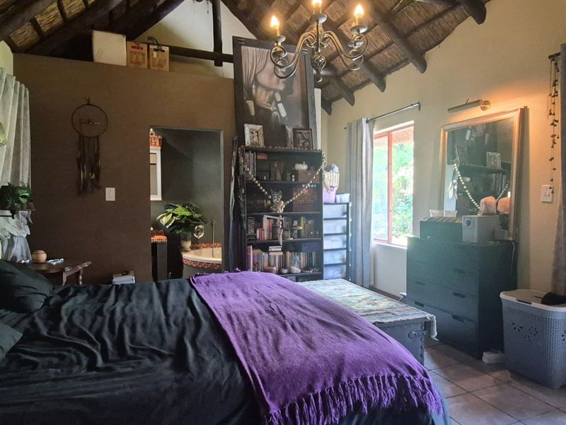 Spacious bedroom featuring a high vaulted thatched ceiling with exposed timber rafters, tiled flooring, and an en-suite bathroom.