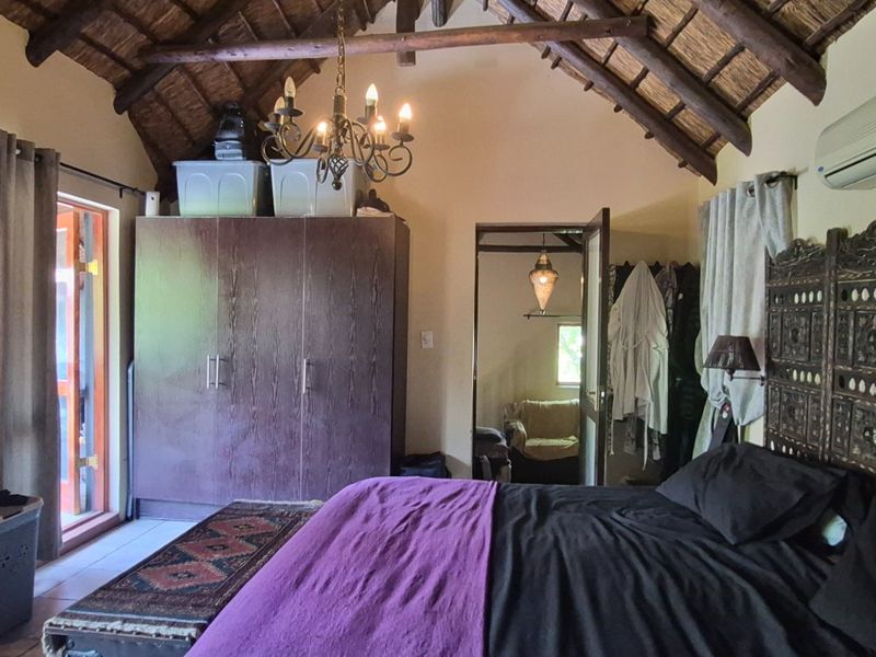 A bedroom featuring a high vaulted thatched ceiling with exposed timber beams, built-in wardrobe, and a wall-mounted air conditioning unit.