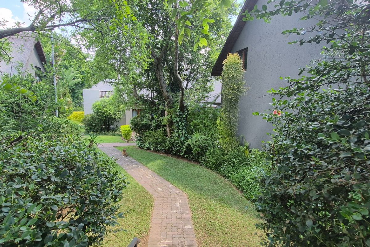 A view of a landscaped garden area with a paved walkway leading between apartment buildings featuring grey stucco exterior walls.