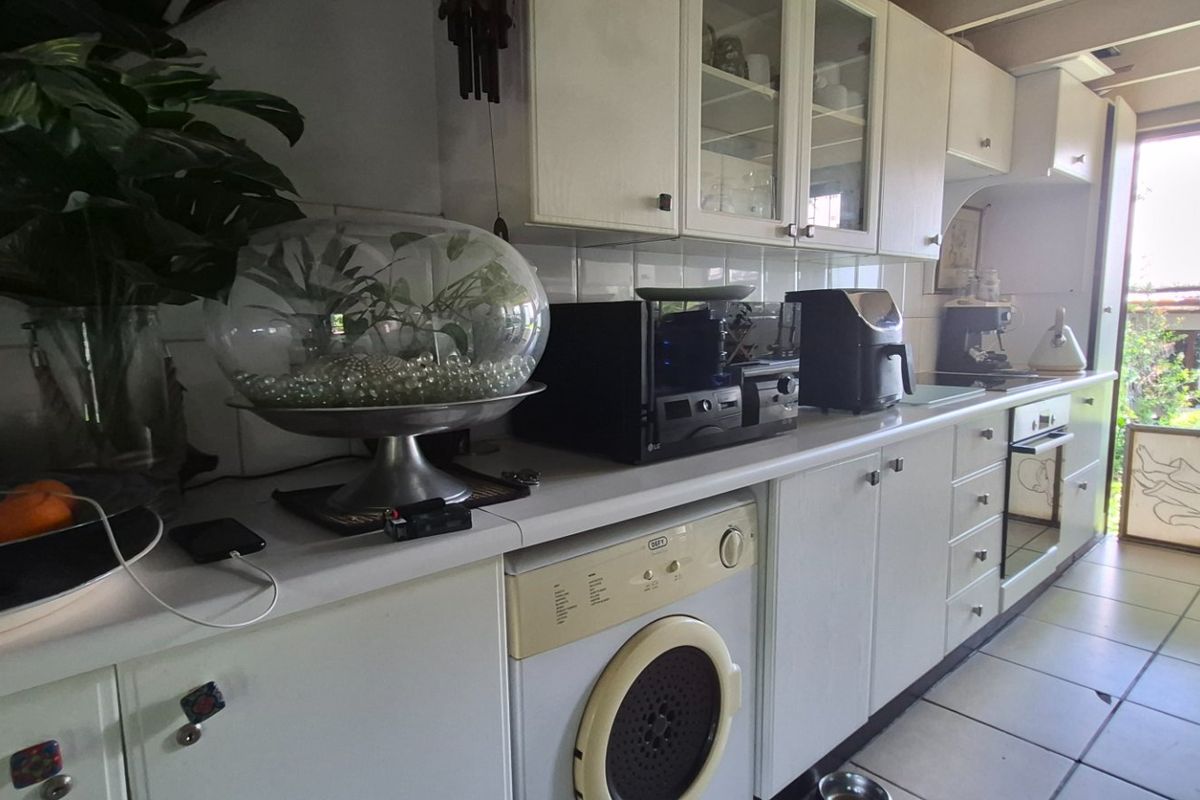 A functional kitchen featuring white cabinetry, tiled backsplash, integrated oven, and built-in laundry appliance with direct access to an outdoor area.