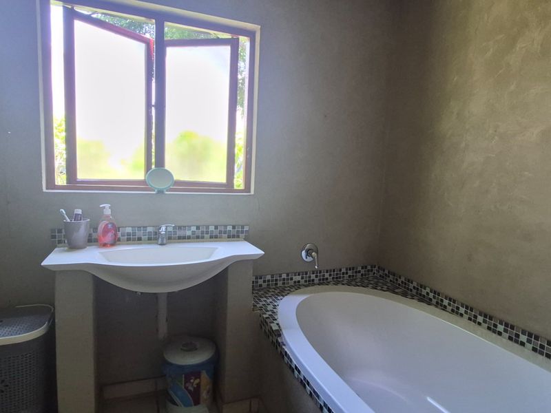 A functional bathroom featuring a built-in bathtub, pedestal washbasin with mosaic tile detailing, and a window providing natural light.