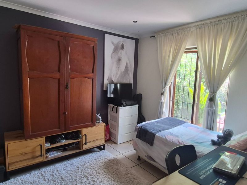 A functional bedroom featuring tiled flooring, recessed lighting, and a sliding glass door with security gate providing access to the exterior.