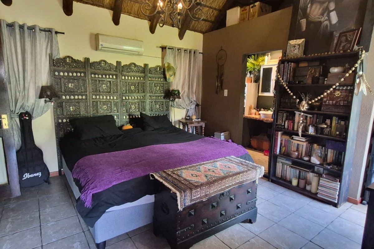Spacious bedroom featuring exposed timber rafters, a thatched ceiling, tiled flooring, and a wall-mounted air conditioning unit.