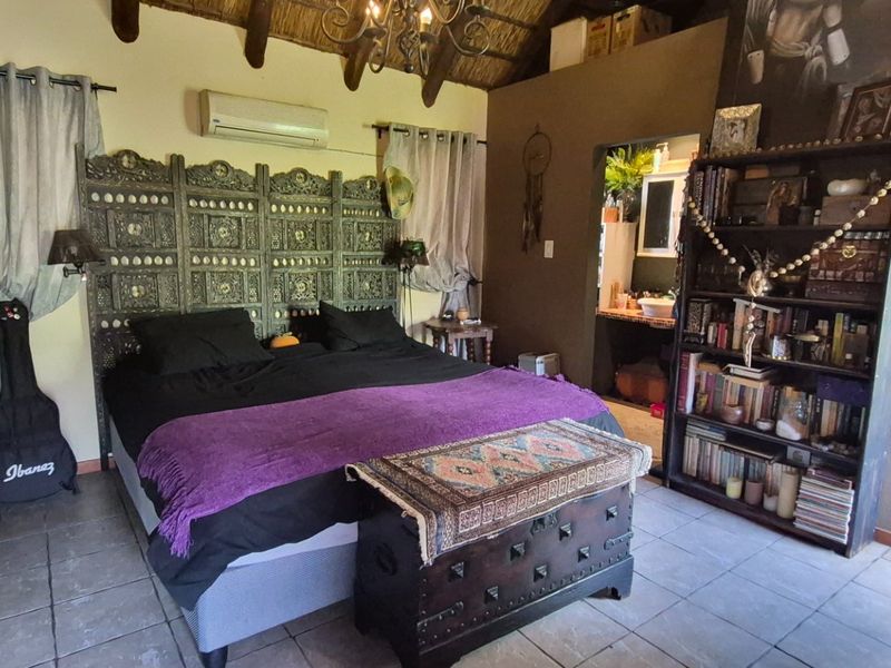 Spacious bedroom featuring exposed timber rafters, a thatched ceiling, tiled flooring, and a wall-mounted air conditioning unit.