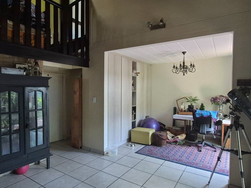 Open-plan living area featuring tiled flooring, a mezzanine level with a wooden balustrade, and integrated built-in cabinetry with recessed shelving.