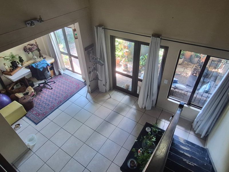 Spacious living area with tiled flooring, large windows, and direct access to the outdoor patio, featuring a staircase with a wooden handrail.